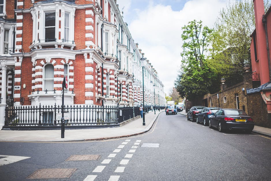 A quiet residential street in Balham with a row of Victorian-style terraced houses featuring red brick facades, white decorative trim, and bay windows. Parked cars line the pavement, including a black
