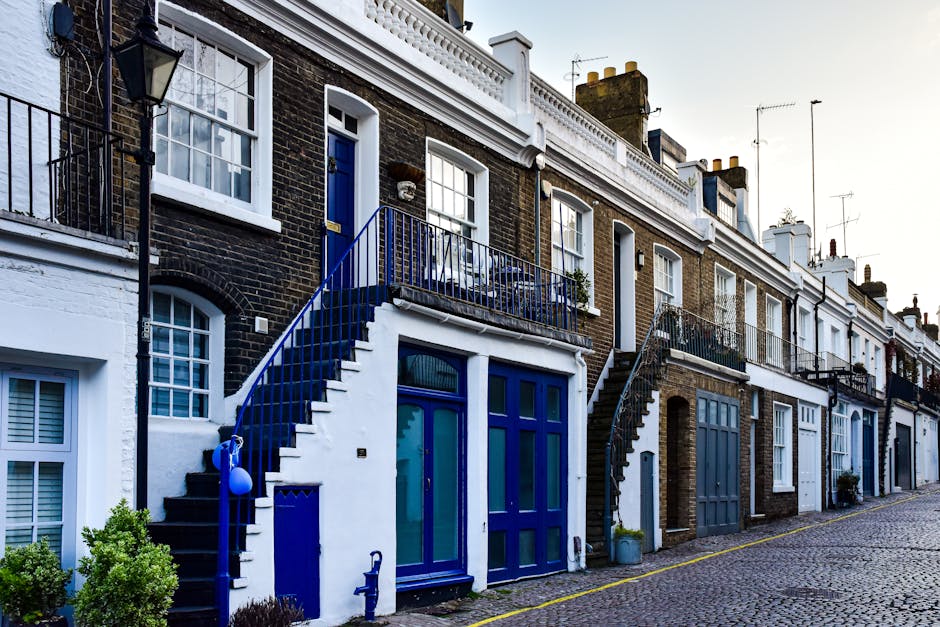 A quiet residential street in Balham with a row of Victorian-style terraced houses featuring red brick facades, white decorative trim, and bay windows. Parked cars line the pavement, including a black